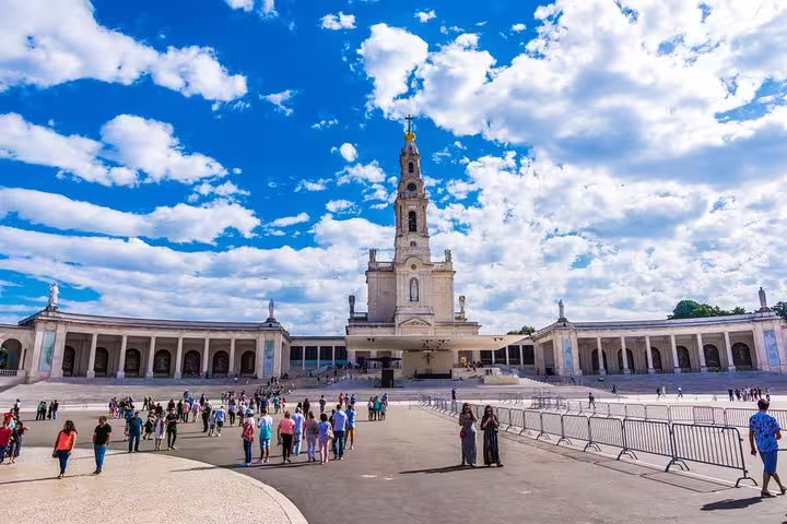 Visitors admire the stunning Fátima Sanctuary under a vibrant sky on a full-day tour from Porto.
