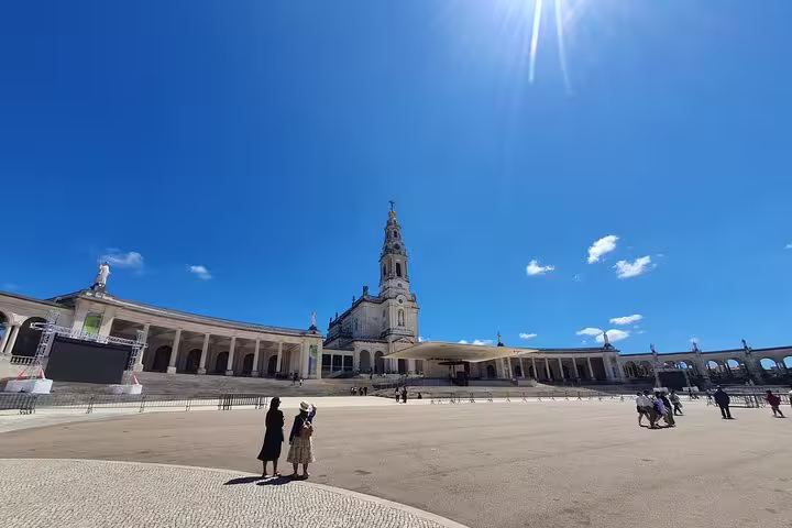 Visitors admire the stunning architecture of the Sanctuary of Fátima under a clear blue sky on the Fátima, Nazaré, Batalha & Óbidos tour.