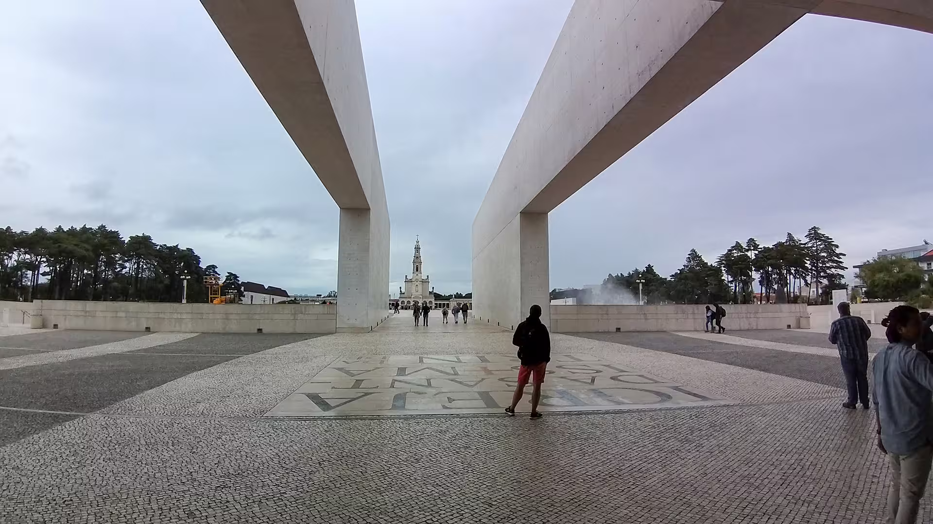 Visitors walk towards the iconic Fátima Sanctuary under modern architectural arches on a private tour in Portugal.
