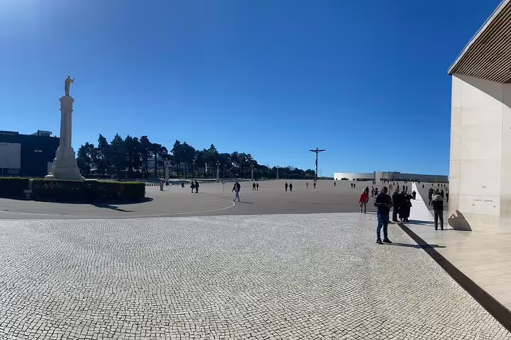 Expansive view of Fátima Sanctuary square under a clear blue sky, highlighting the monumental cross and statue.