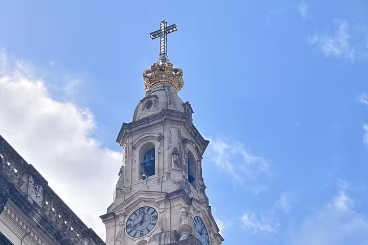 Tower of the Sanctuary of Our Lady of Fatima with golden crown and cross against a blue sky, highlighting religious significance.