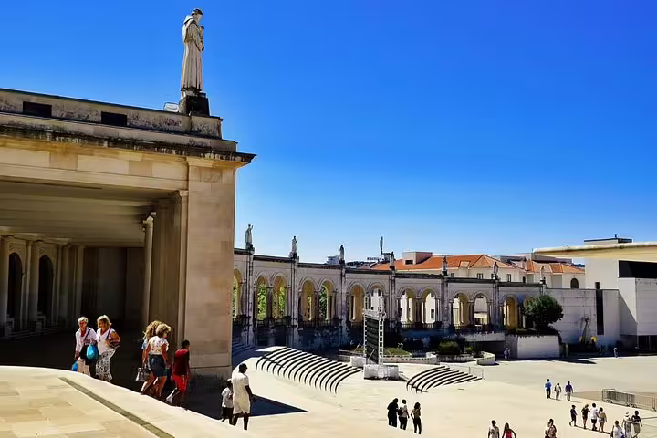 Visitors exploring the expansive grounds of the Fatima Shrine, surrounded by elegant colonnades and vibrant blue skies.