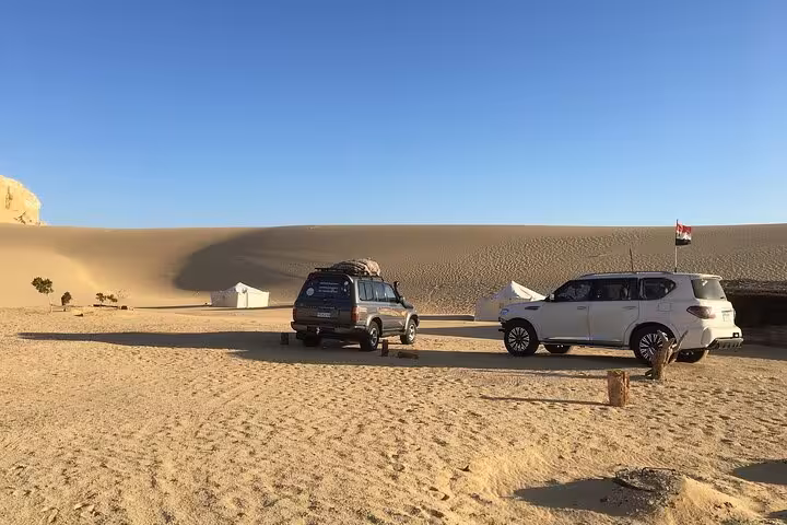 Two jeeps parked on sandy desert terrain during a Fayoum Oasis private tour from Cairo, under a clear blue sky.