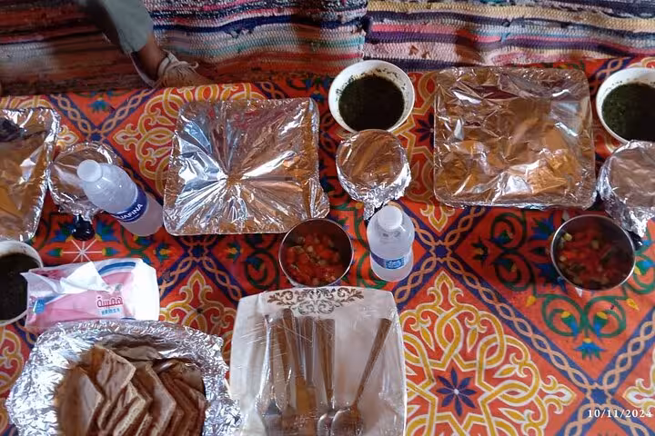 Traditional Egyptian meal with various dishes and drinks served on vibrant patterned tablecloths at Fayoum Oasis tour.