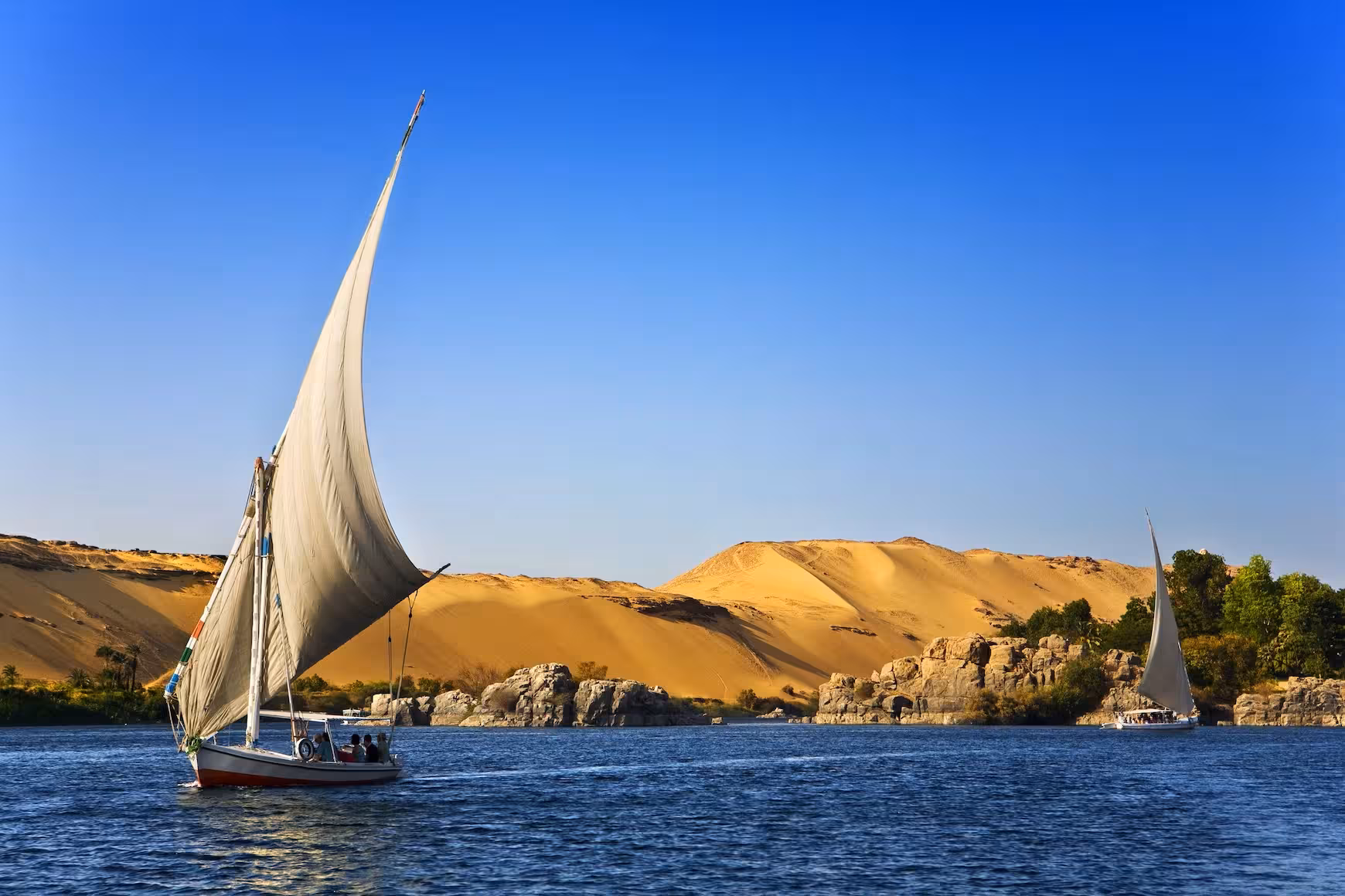 Felucca sailing on the Nile near Aswan desert dunes, scenic view for Classic Egypt 5-star Nile cruise tour