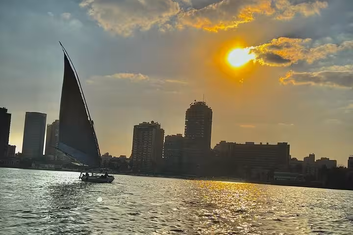 Traditional felucca sailboat cruising the Nile River in Cairo at sunset, with city skyline in view