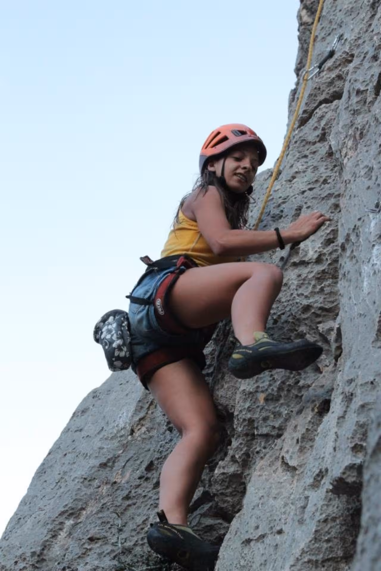 Female climber tackling a vertical rock wall in Fuili Canyon, wearing safety gear, highlighting thrilling climbing tour.