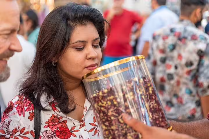 Female traveler smelling fragrant hibiscus tea at a lively Dubai spice market during a guided walking food tour
