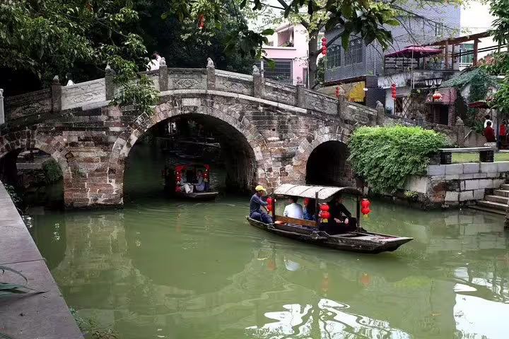 Quaint stone bridge arches over tranquil canal with wooden boats in Fengjian Water Town, a highlight of Shunde tours.