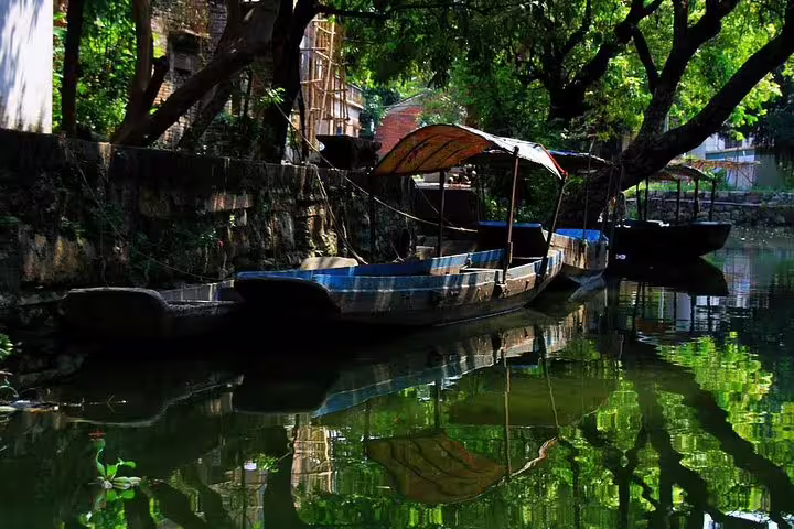 Traditional boat moored along serene canal in Fengjian Water Town, Shunde, surrounded by lush greenery and reflections.