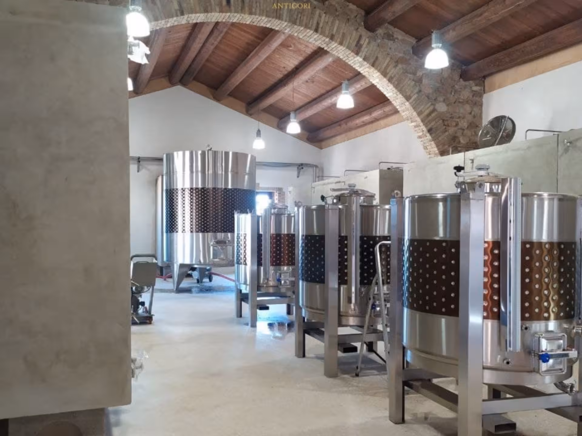 Modern stainless steel fermentation tanks inside a rustic winery in Cagliari countryside.