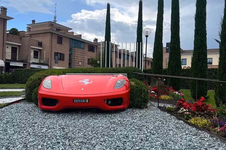 Experience the unique Ferrari sculpture garden showcasing a red sports car front amidst lush landscaping and vibrant flowers.