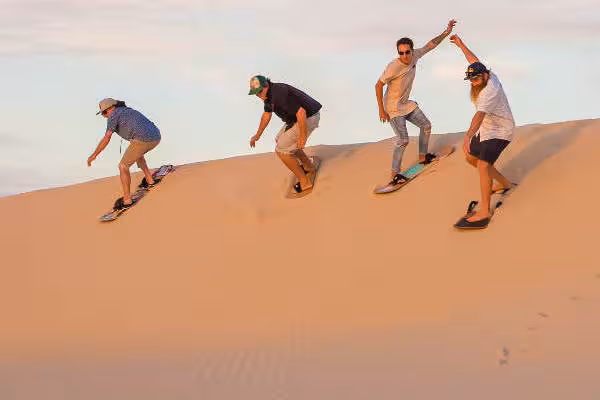 Group enjoying sandboarding on Merzouga dunes during a 4-day Fes to Errachdia desert tour.