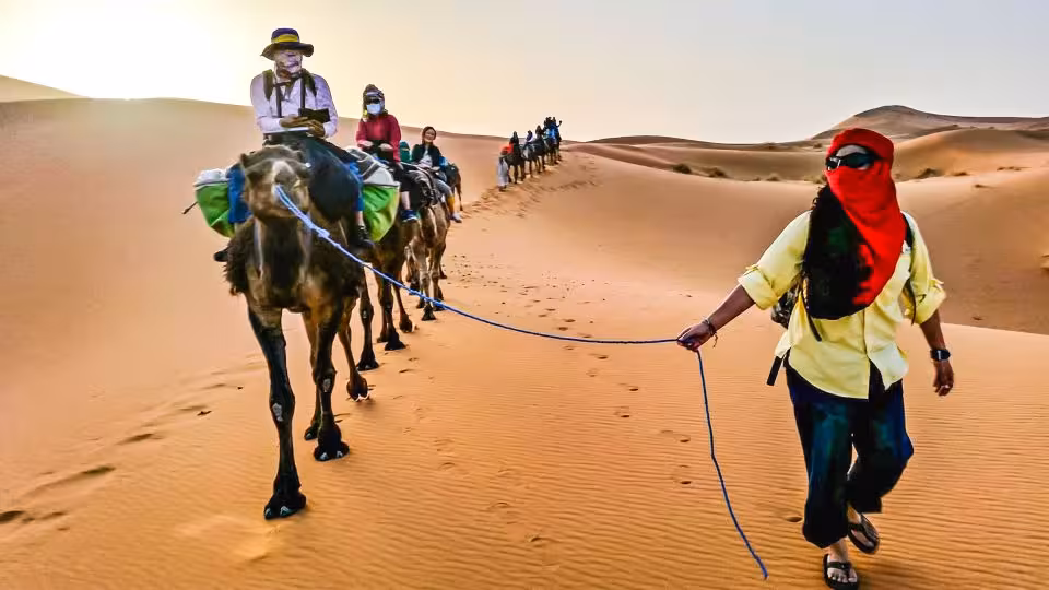 Tourists enjoy a camel trek across the stunning dunes of Merzouga desert during a 4-day Fes to Marrakech tour.
