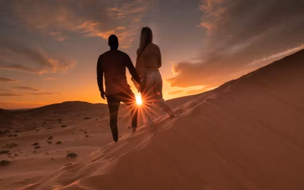 Couple holding hands on a sand dune at sunset during a private desert tour from Fes to Merzouga Erg-chebbi.