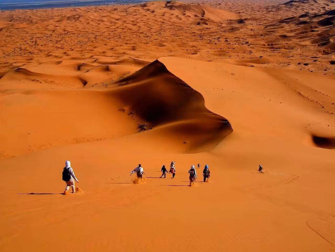 Travelers trekking down the vast, sunlit dunes of Erg Chebbi on a 4-day adventure starting from Fes.