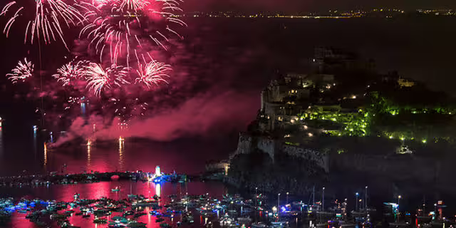 Fireworks over Ischia’s Aragonese Castle during Festa di Sant’Anna, with illuminated boats and reflections on the bay at night