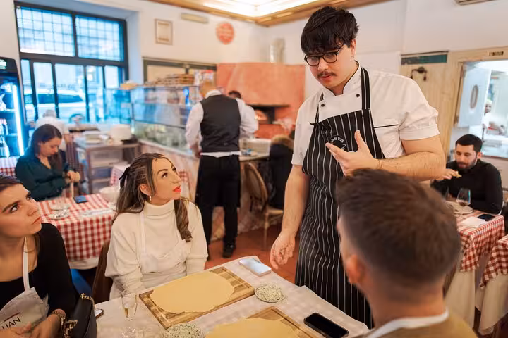 Chef instructing participants at a fettuccine pasta cooking class in a cozy Rome city center restaurant.