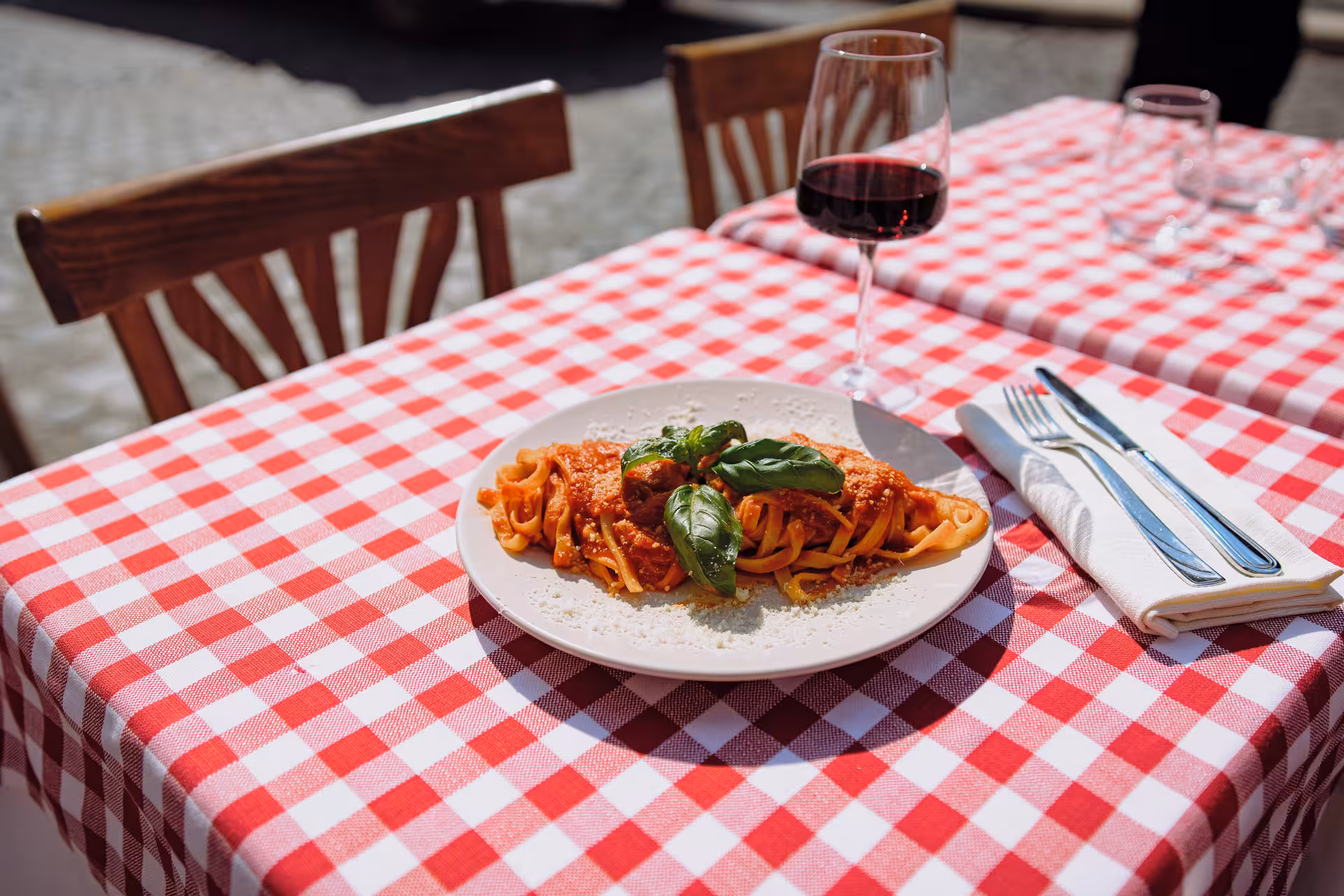 Plate of fettuccine with tomato sauce and basil on a checkered tablecloth in Rome city center.