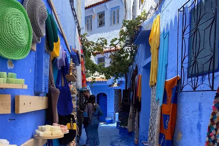 Charming blue street in Chefchaouen lined with vibrant textiles and local goods on a full-day tour from Fez.