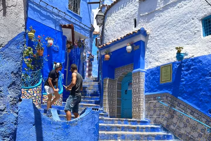 Tourists exploring the vibrant blue alleys of Chefchaouen, adorned with colorful flower pots and intricate tiles.