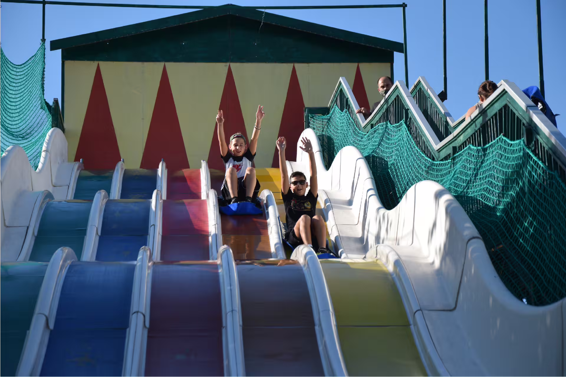 Kids sliding down colorful multi-lane slide at Fiabilandia Rimini, Italy, with amusement park entry ticket