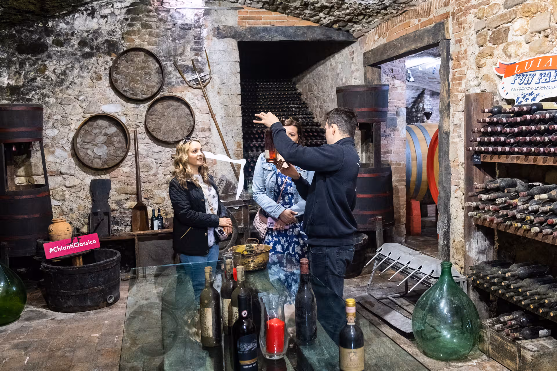Wine expert explaining vintage bottles in a rustic Chianti Classico cellar on a private FIAT 500 wine tour.