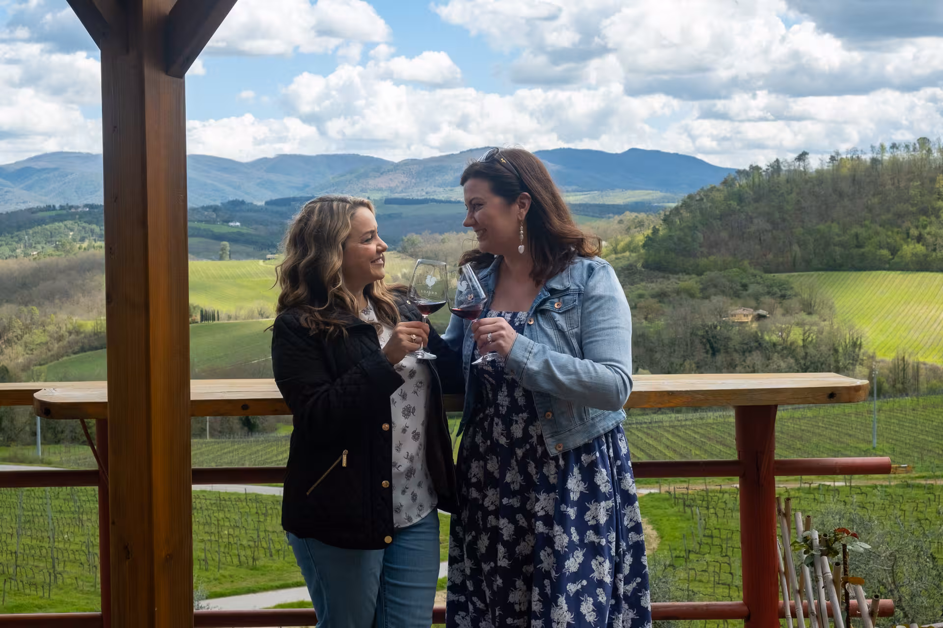 Two women enjoying a wine toast with a scenic view of Chianti Classico vineyards during a vintage FIAT 500 tour.