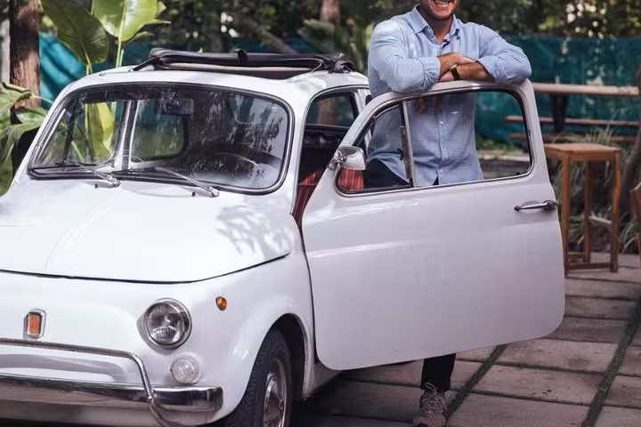 Man leaning on a classic white Fiat 500 with open door, showcasing vintage charm for a Sorrento wine tour.