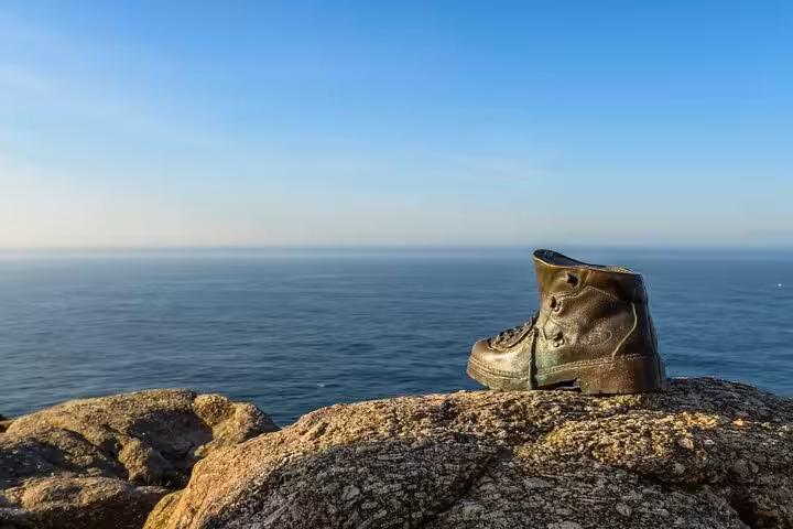 Solitary boot on rocky cliff edge with panoramic view of the Atlantic Ocean at Finisterre, under clear blue skies.
