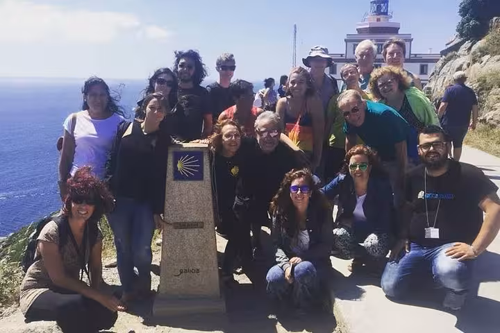 Group of tourists at Finisterre lighthouse enjoying the scenic view during the Costa da Morte excursion.