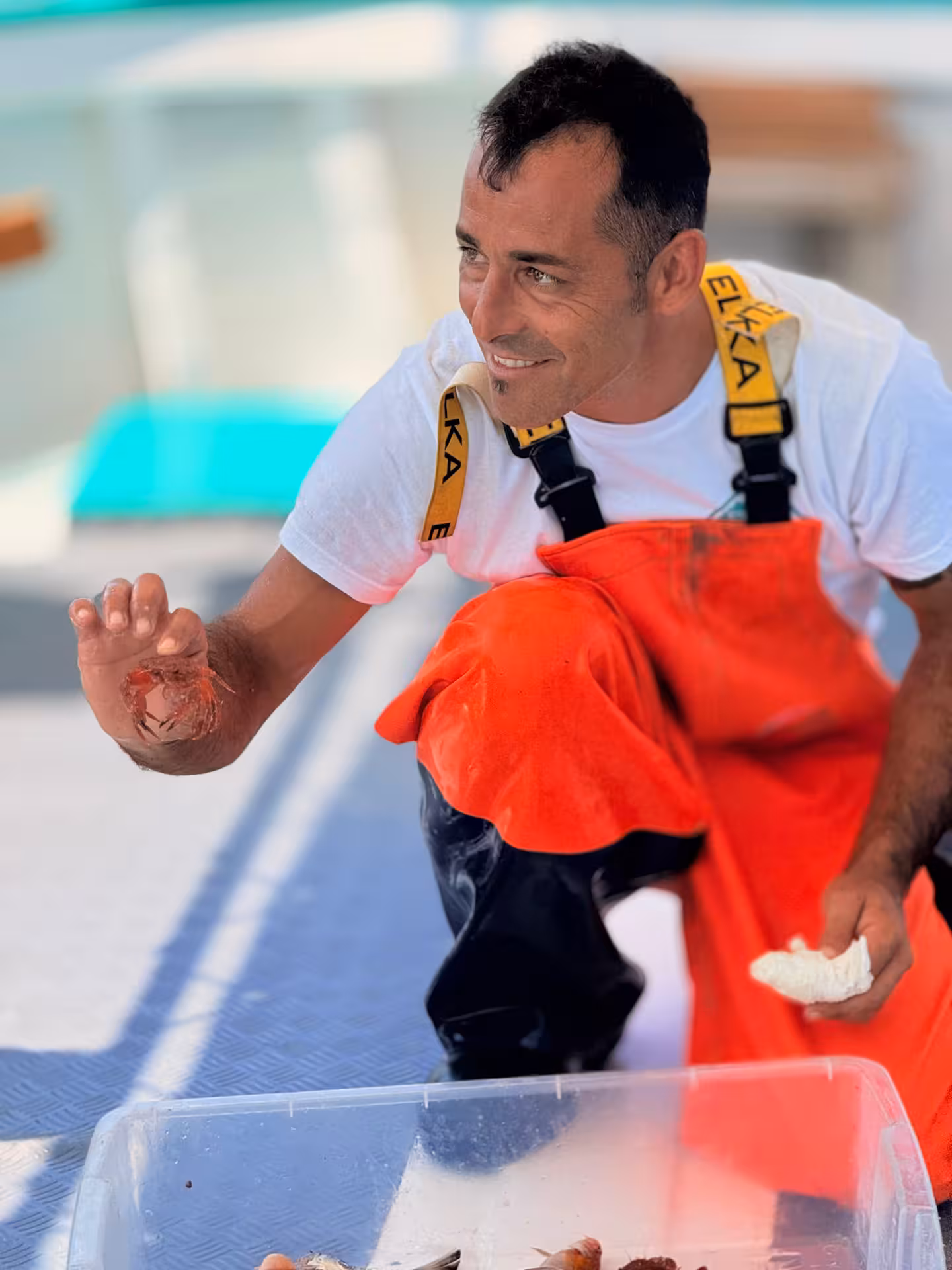 Smiling fisherman in orange overalls showing a crab during an Asinara Park boat tour.