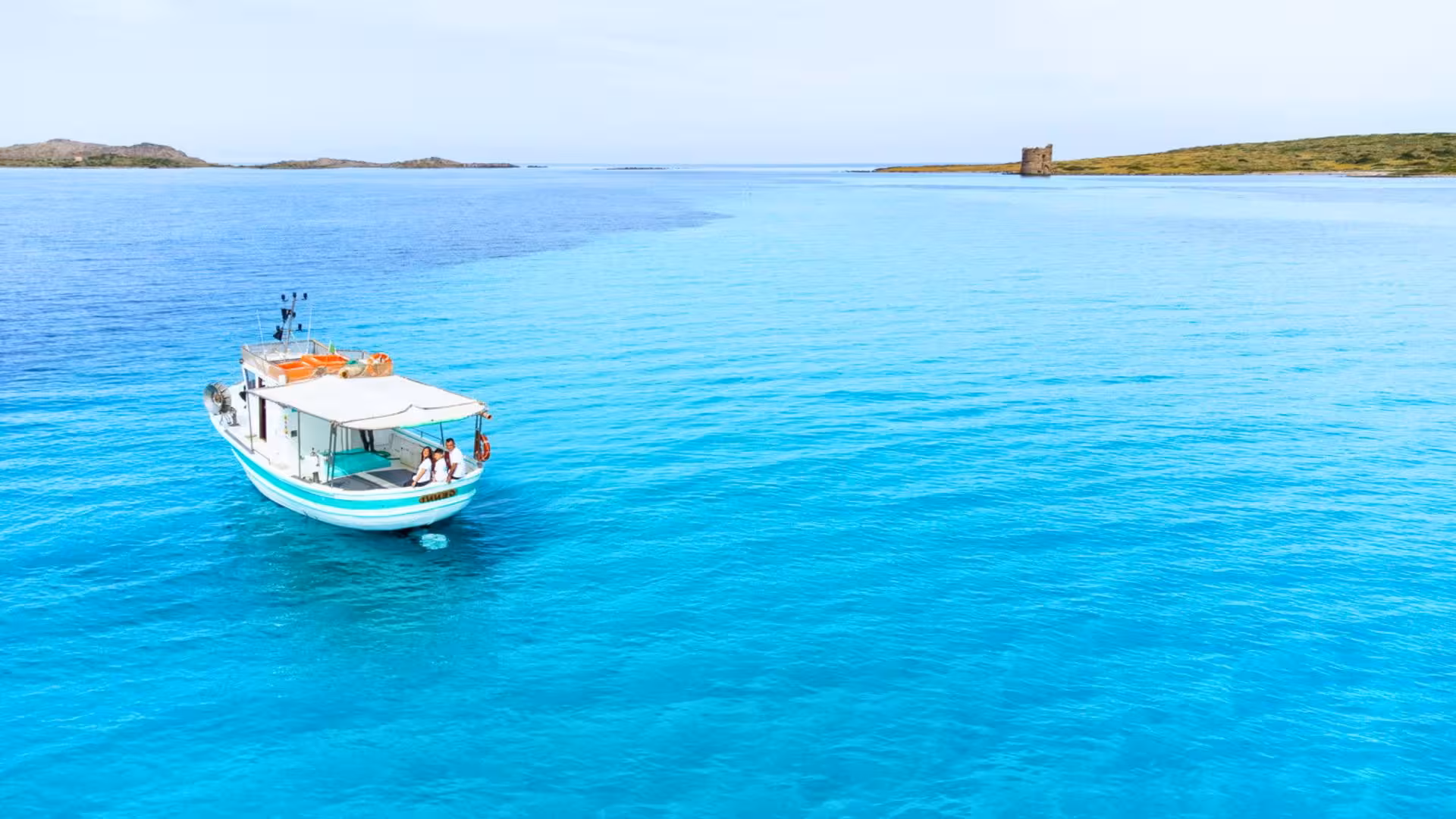 Fishing boat in Asinara Park's turquoise waters with historic tower in the distance, offering scenic Stintino tours.