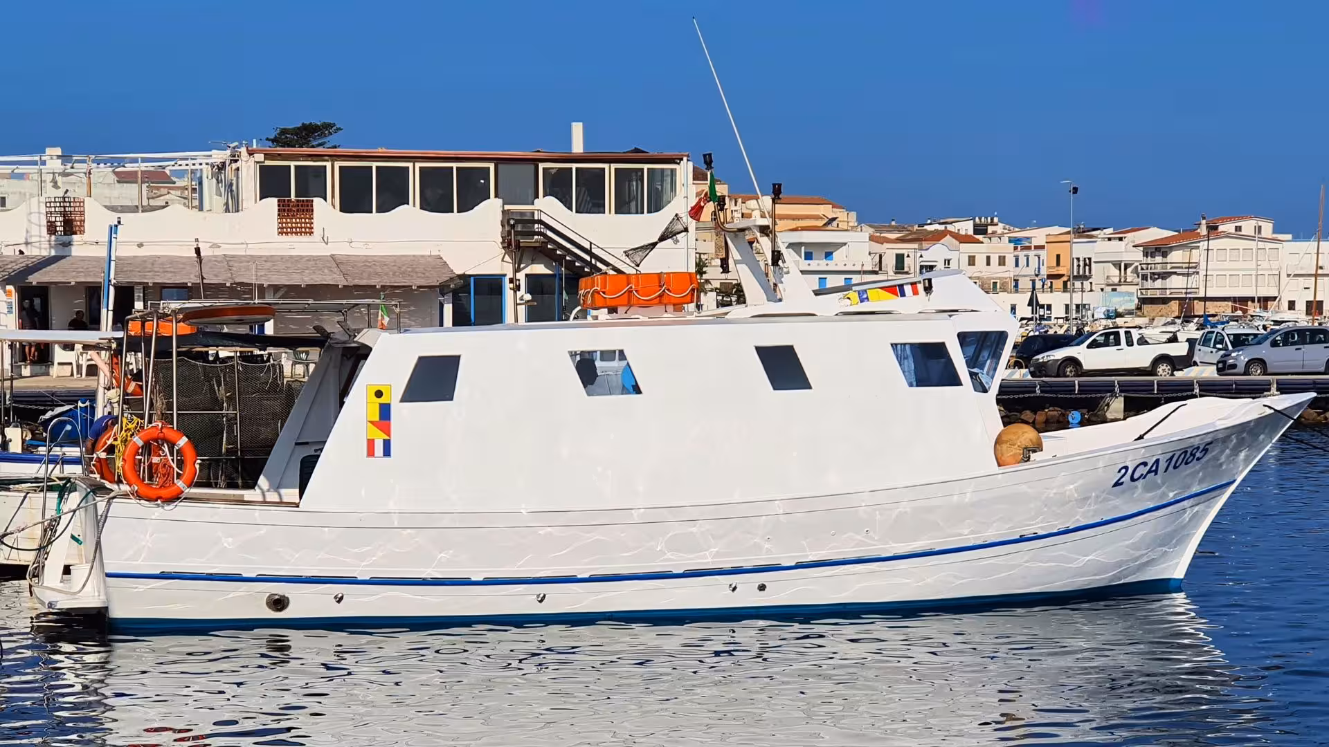 White fishing boat docked at Calasetta port for San Pietro Island tour under a clear blue sky.