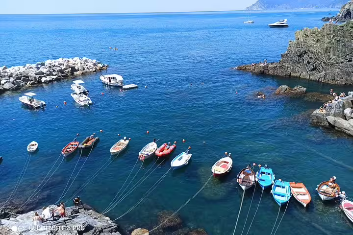 Moored fishing boats on the clear blue Ligurian Sea near rocky cliffs along the Cinque Terre coast on a private Porto Venere tour