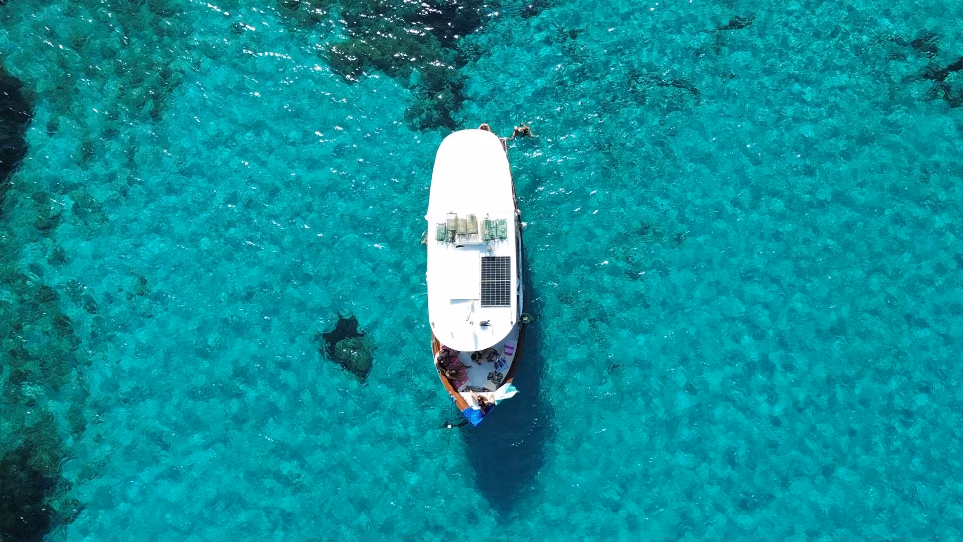 Aerial view of a boat on the crystal-clear waters near Tavolara during a fishing tourism excursion from San Teodoro.