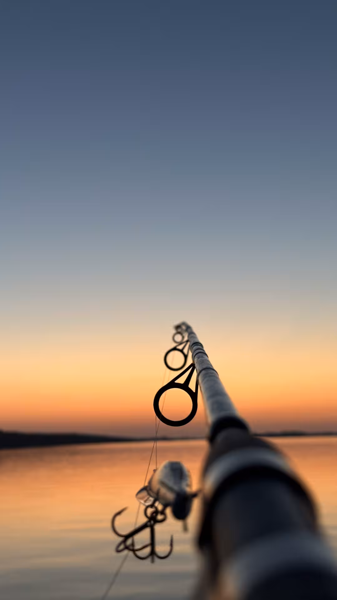 Fishing rod and lure silhouetted at sunset over tranquil water, catch of the day evening fishing experience