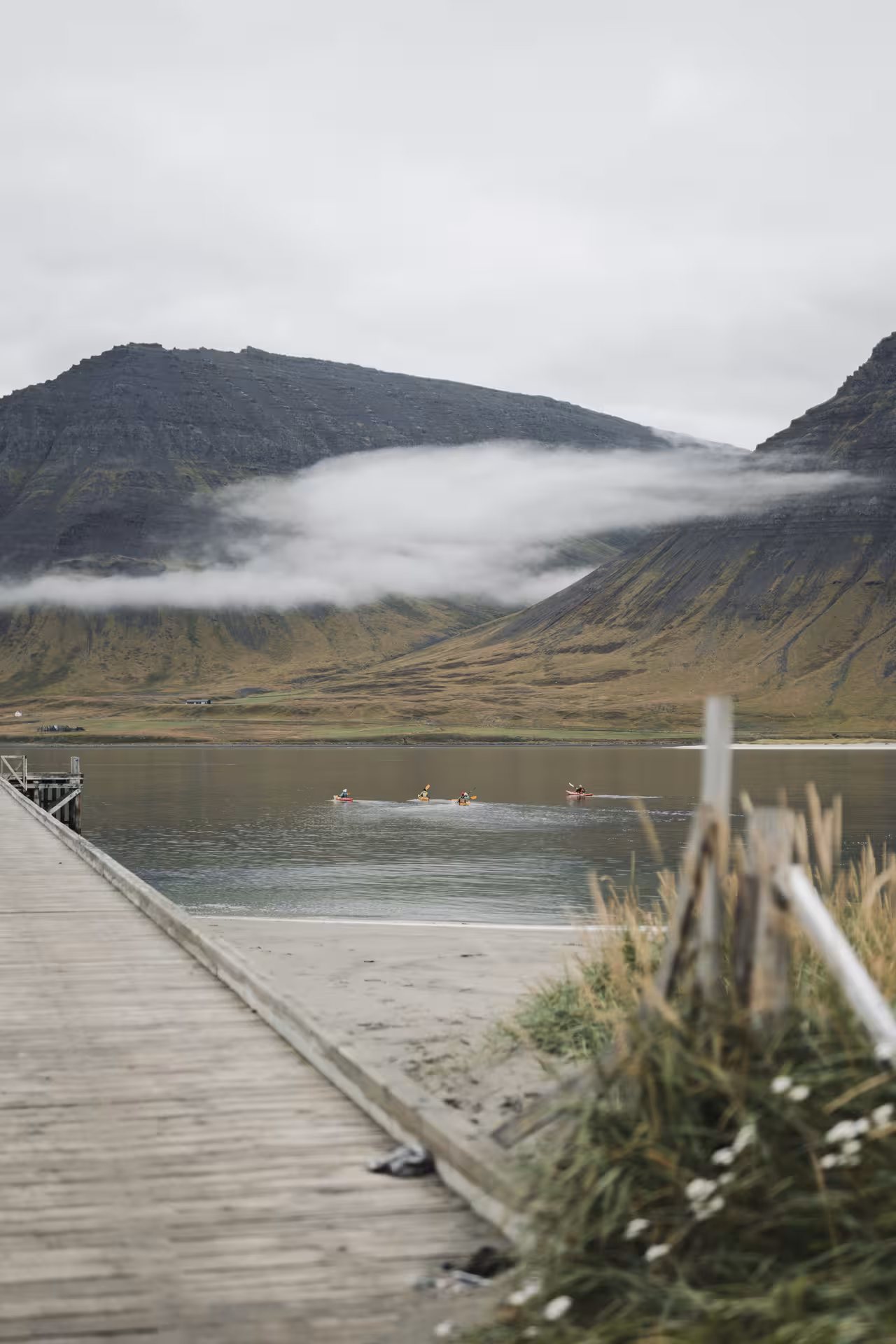 Kayakers paddling across a calm fjord beneath misty mountains near a pier on a Fjord Discovery sea kayaking tour