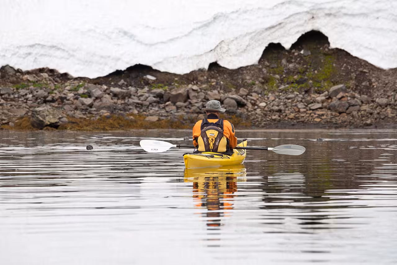 Solo kayaker gliding on calm fjord waters near snowfields, Fjord Discovery sea kayaking tour in the Arctic