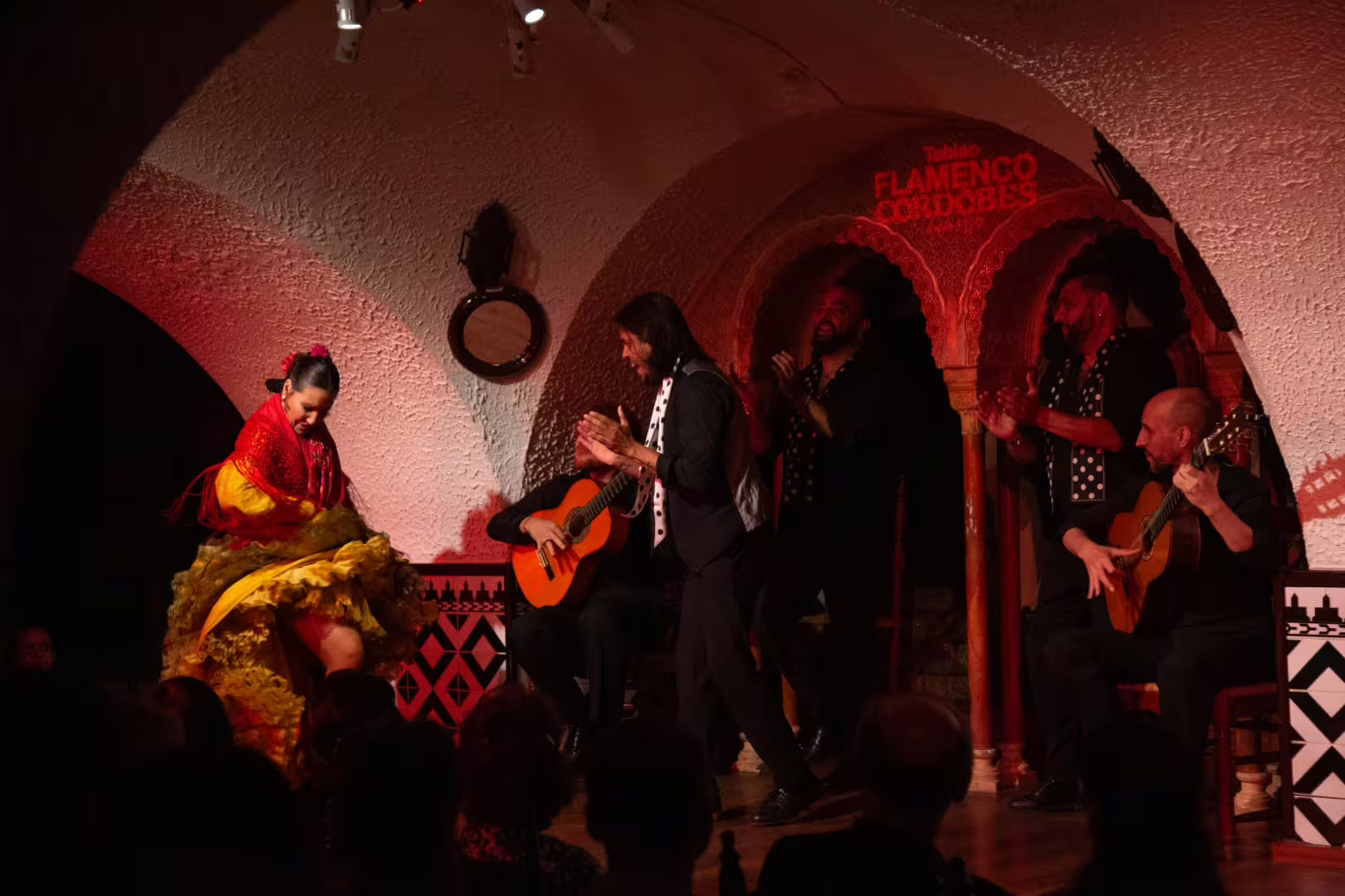 Dynamic flamenco dancer in red and yellow dress performs at Tablao Cordobes in Barcelona with live guitar music.