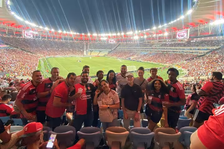 Tour group enjoying Flamengo game at Maracanã Stadium, Rio de Janeiro, with packed stands and bright stadium lights