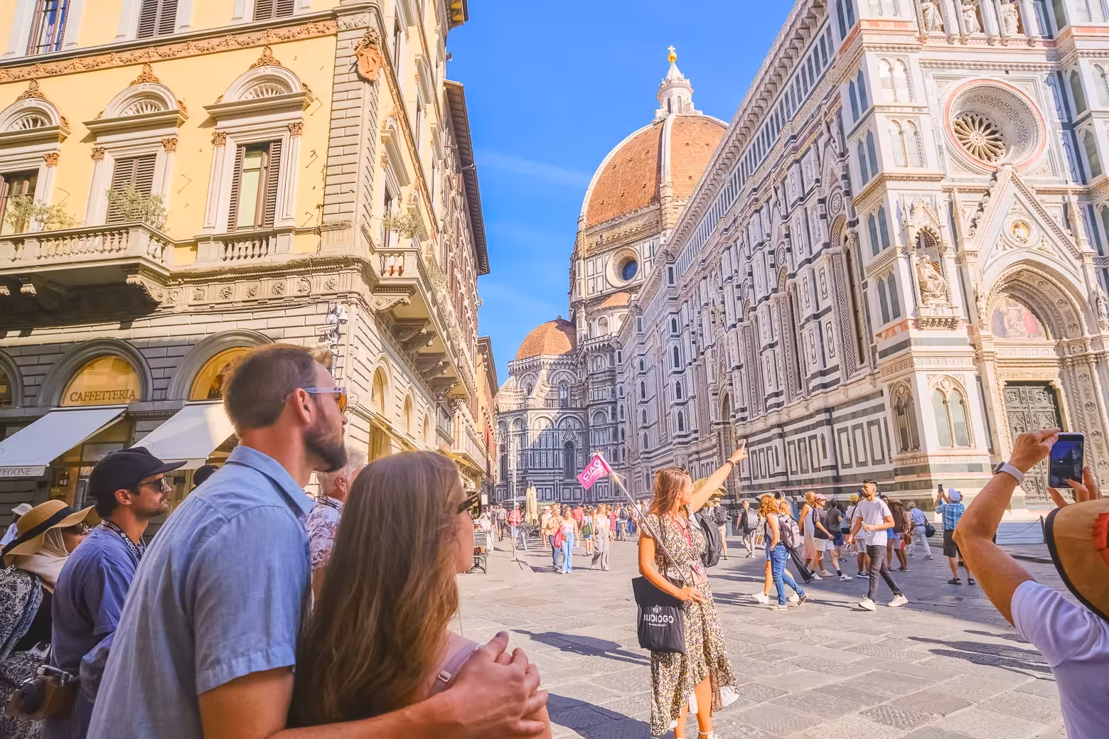 Tourists admire the stunning exterior of Florence Duomo Cathedral during a skip-the-line guided tour under a clear blue sky.
