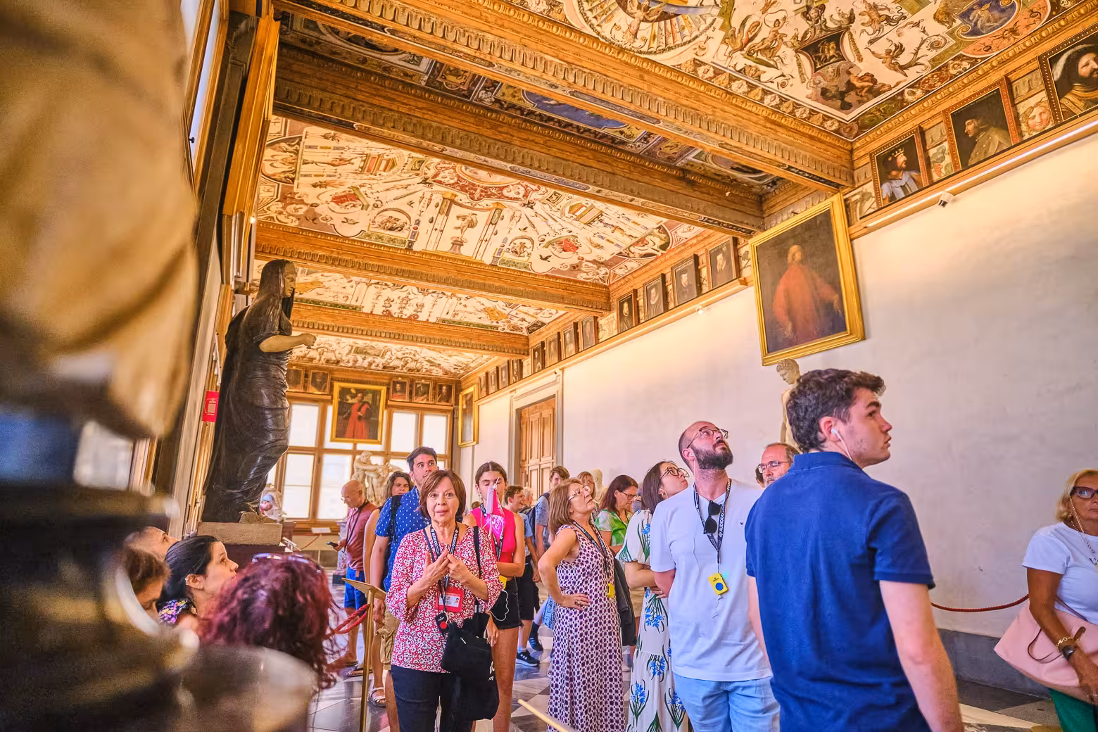 Tourists admiring the ornate ceilings and art during a guided tour at Florence's Uffizi Gallery.