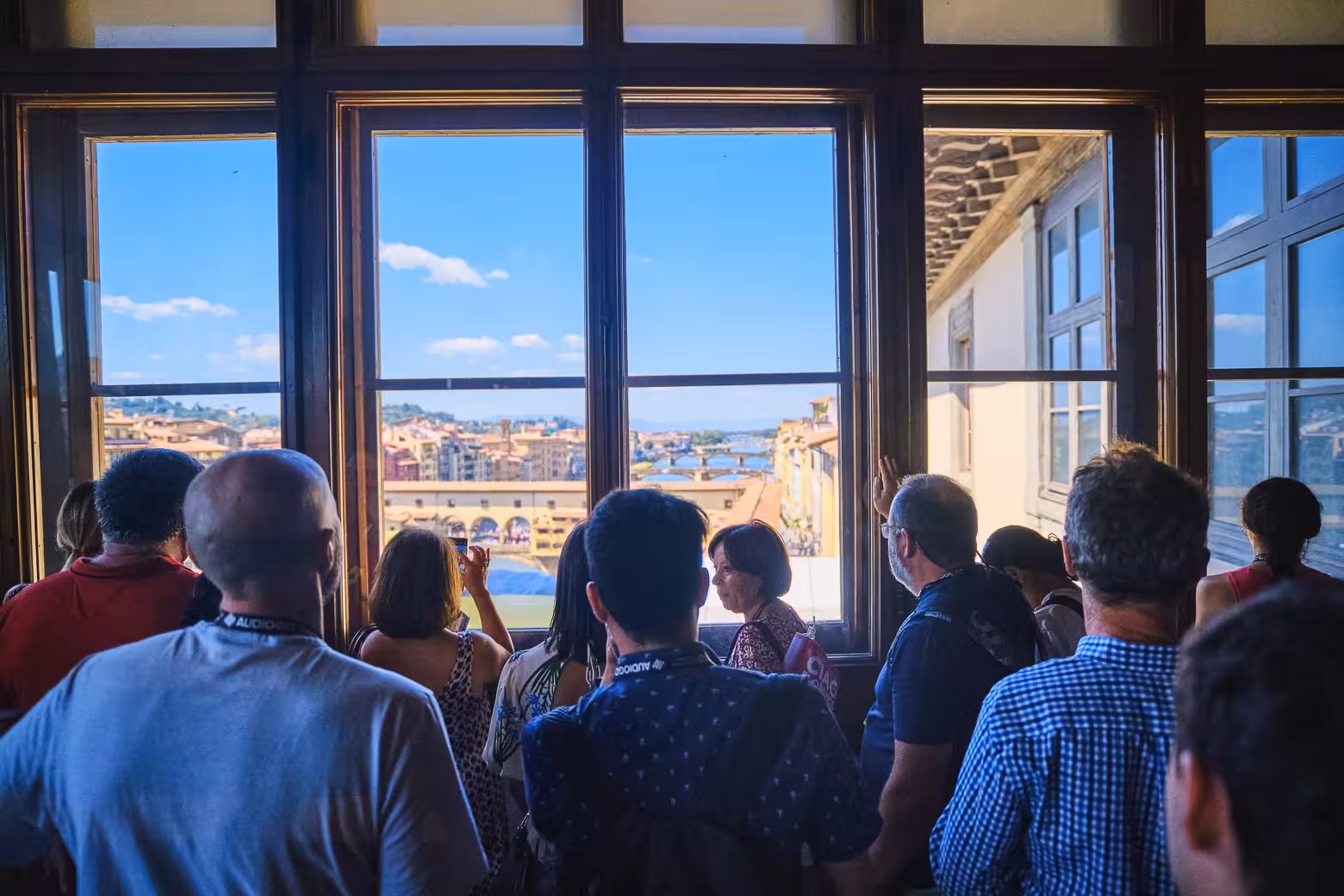 Tourists enjoying a panoramic view of Florence from a window inside the Uffizi Gallery during a guided tour.
