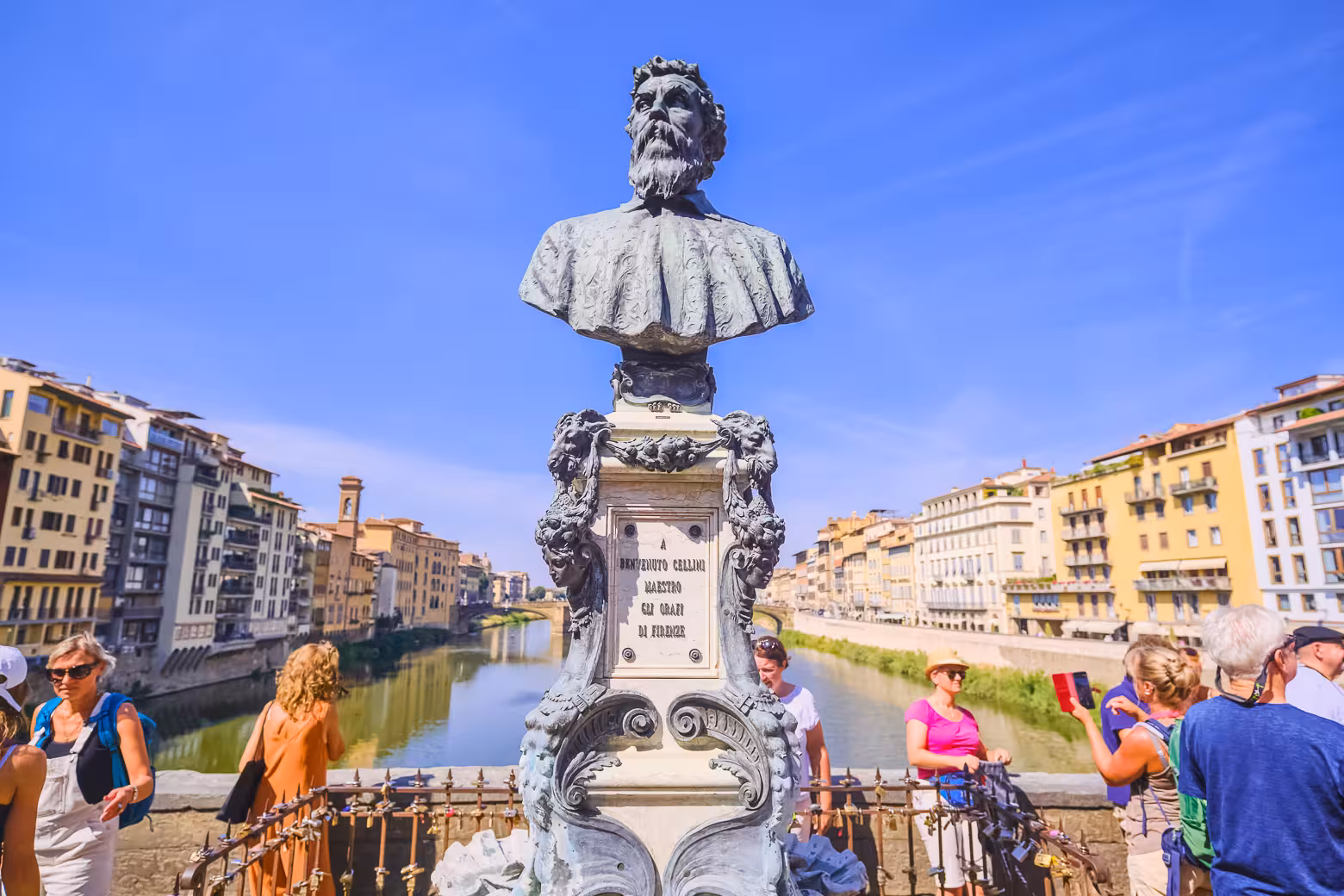 Bust of Benvenuto Cellini on Ponte Vecchio with tourists enjoying views of the Arno River in Florence.