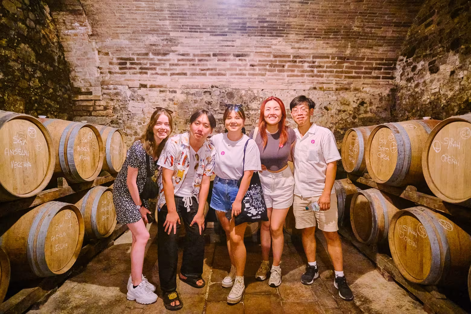 Group of friends smiling by wine barrels in a Florence cellar during an exclusive wine tasting experience.