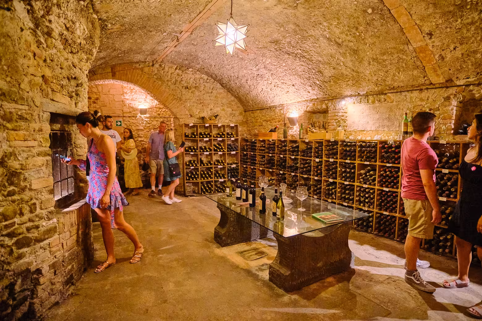 Visitors exploring a rustic wine cellar in Florence, filled with rows of vintage wine bottles.
