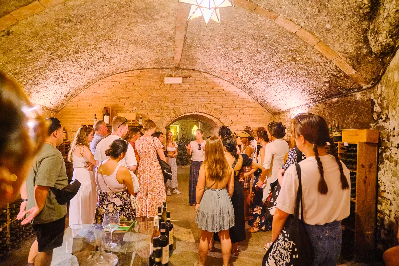 Tour group enjoying a wine tasting experience in a rustic Florence wine cellar with brick arches.
