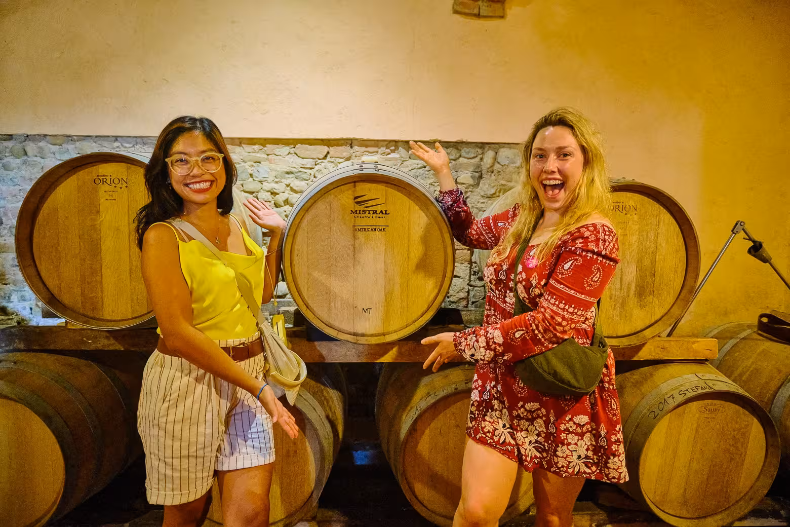 Two excited tourists posing by wine barrels during a Florence small-group wine tasting tour.