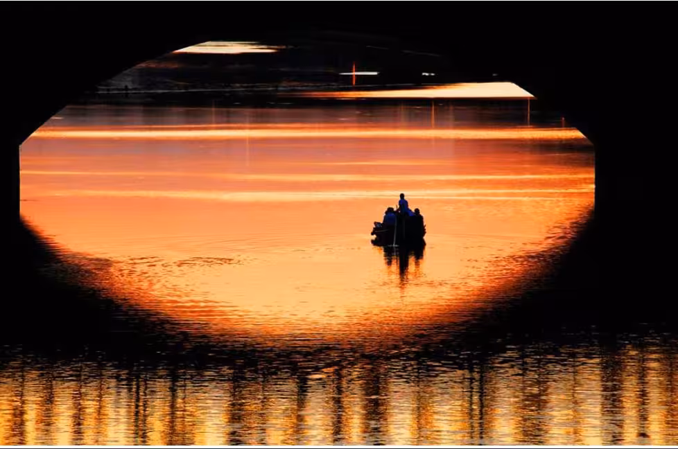 Florentine gondola glides under a bridge at sunset, casting silhouettes on the serene waters of Florence.